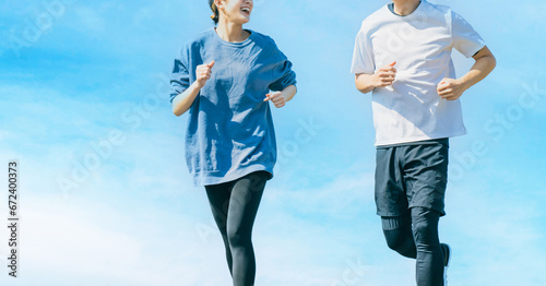 青空の下でジョギングをする笑顔の日本人男女 photo
