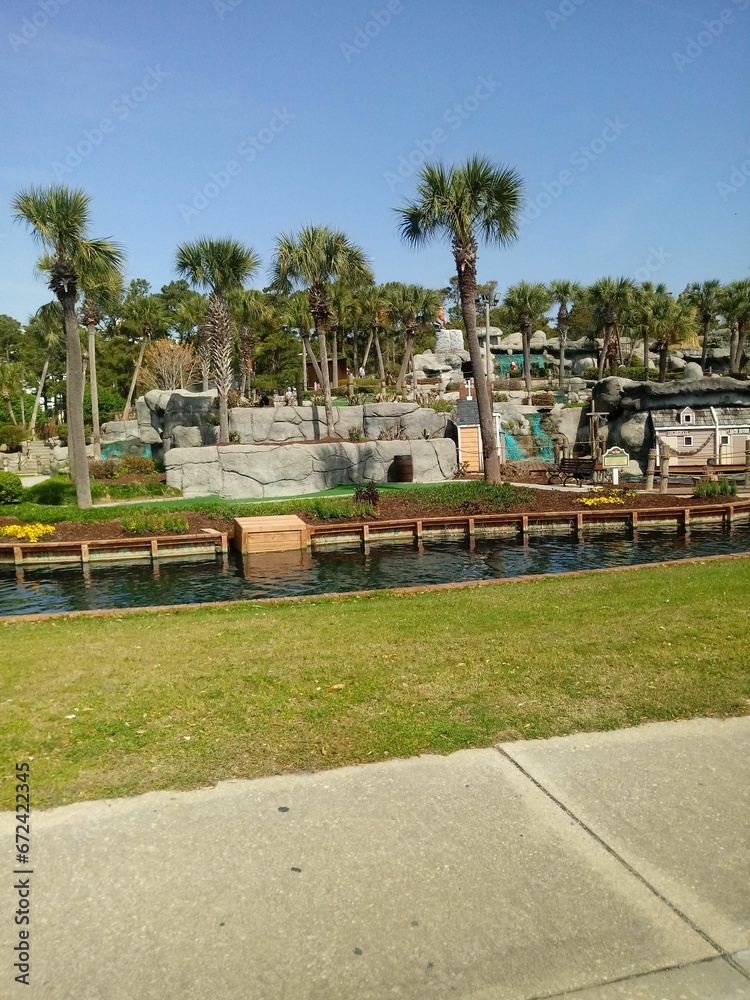 a small waterfall with a wooden bridge over it in front of palm trees