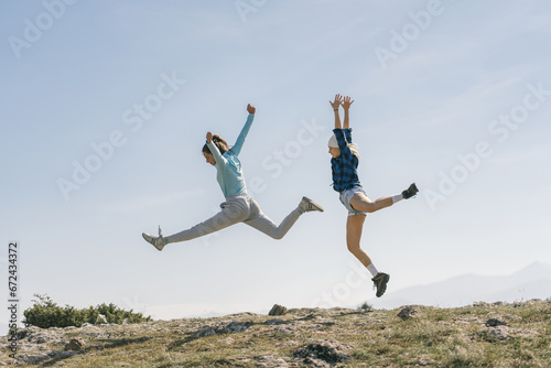 Pretty female hikers jumping and having fun on top of the mountain early in the morning