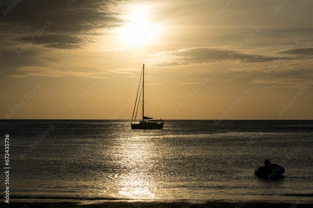 Fototapeta premium Small vessel sailing across the ocean at sunset