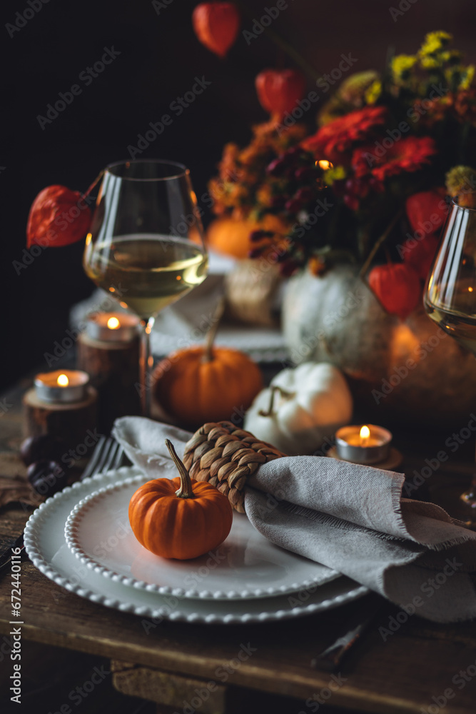 Fototapeta premium Cozy festive holiday table decor for home family Thanksgiving dinner. Traditional event, elegant natural decoration. Wooden rustic table, countryside style. Burning candles, floral centrepiece pumpkin