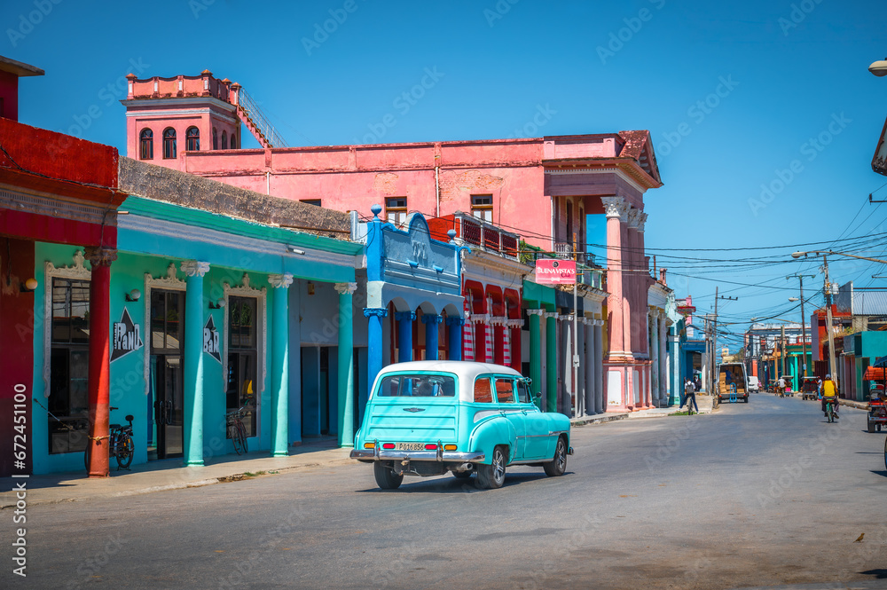 Moron, Diego de Avila Province, Cuba - February 23 2023: Turquoise vintage car in the street of the city of Moron, bike on street, colourful shops.