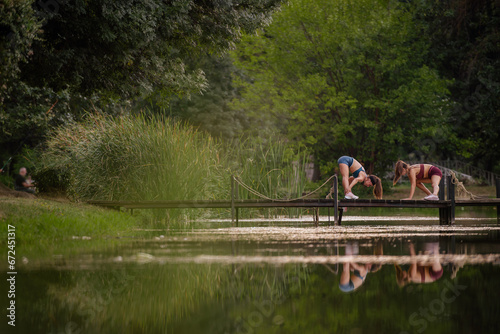 Fit females warm up, exercising on bridge in park. Active, attractive bodies, stretching arms and legs. Sporty, healthy lifestyle in green environment, outdoors. Gorgeous nature scene, muscular built.
