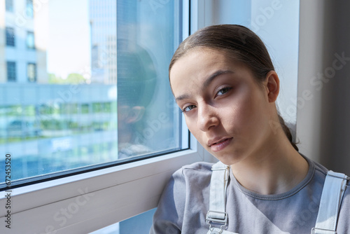 Headshot portrait of teenage serious girl looking at camera, at home