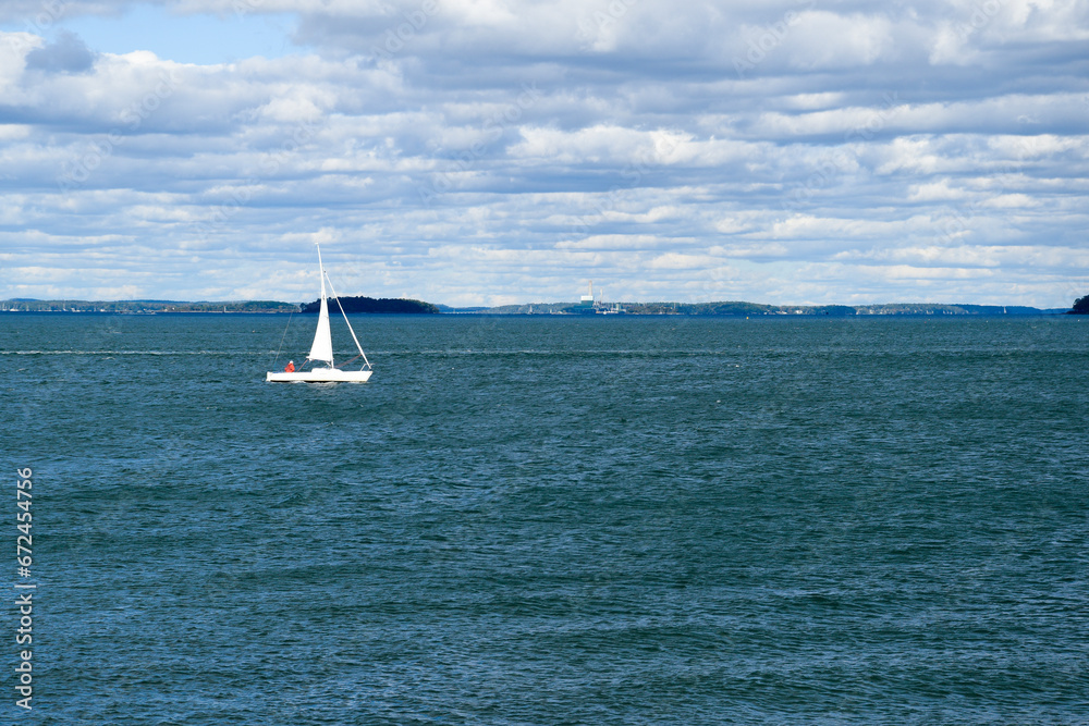 White sailboat isolated on blue ocean water and cloudy sky. Single boat sailing in choppy water.