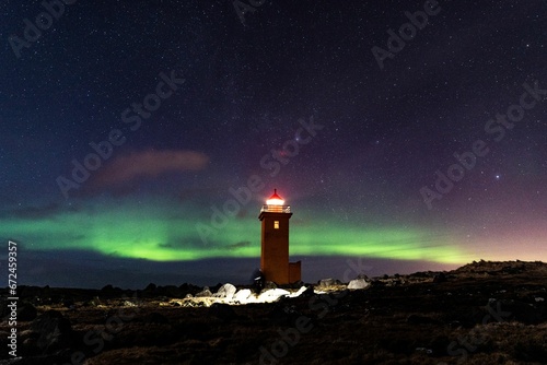 Majestic lighthouse stands on a rocky shoreline, illuminated by an ethereal light of an aurora