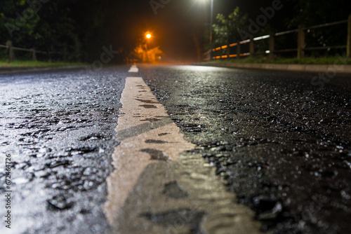 A low angle shot of an empty road on a misty night with street lights and a shallow depth of field.