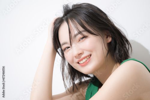 座って髪をかき上げる女性 カメラ目線の顔のクローズアップの笑顔 ヘアケアや美容のイメージ