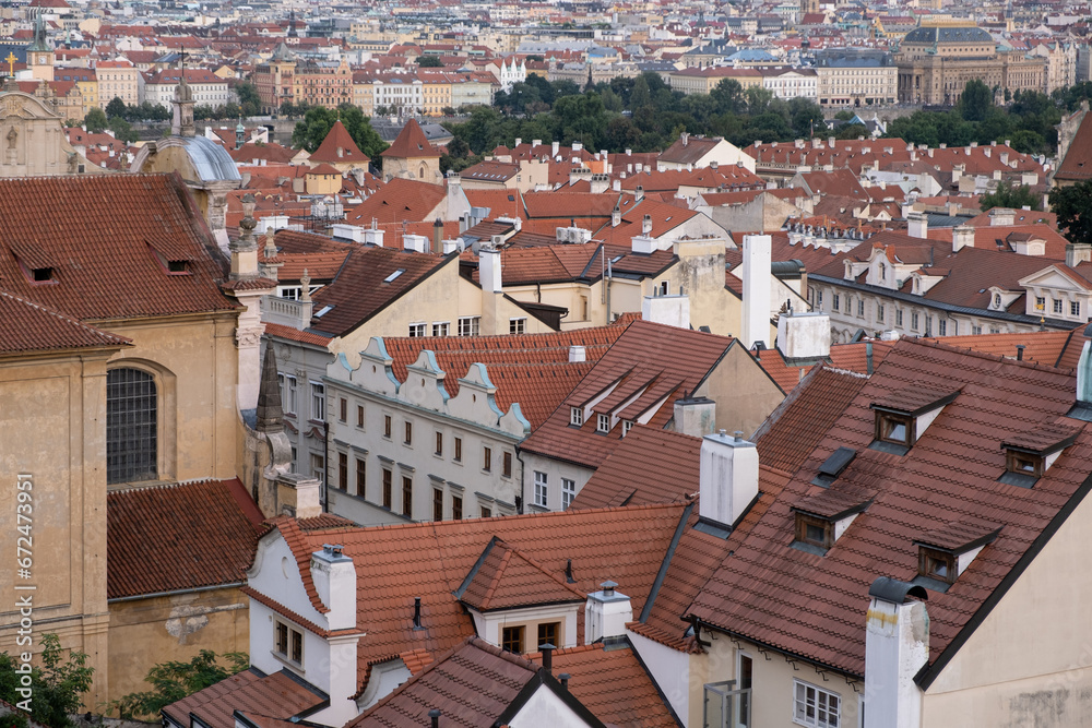 picturesque view of the old town in Prague, featuring rooftops with aged tiled covers and brick chimneys. The red-tiled roofs