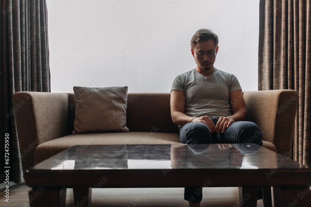 Lonely asian man sits on the sofa thinking of his lover. Lonely asian man sits on the sofa thinking of his lover.