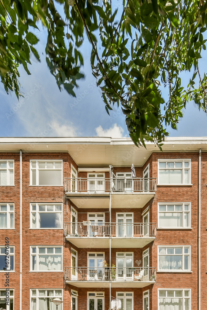 Fototapeta premium a brick apartment building with balks on the balcony and green trees in the fore - swayr stock photo