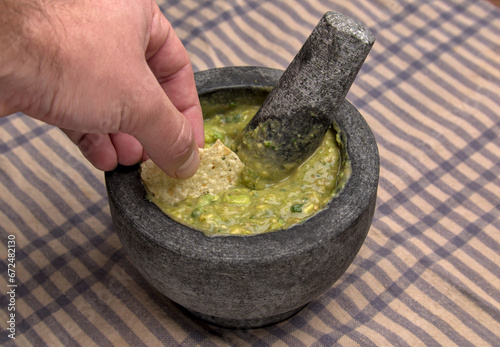 hand dipping tortilla chip into guacamole inside molcajete (traditional mexican mortar and pestle for grinding spices and making sauces) spicy avocado dip with aztec roots (man, white, caucasian)