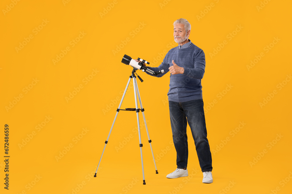 Senior astronomer with telescope showing thumb up on yellow background