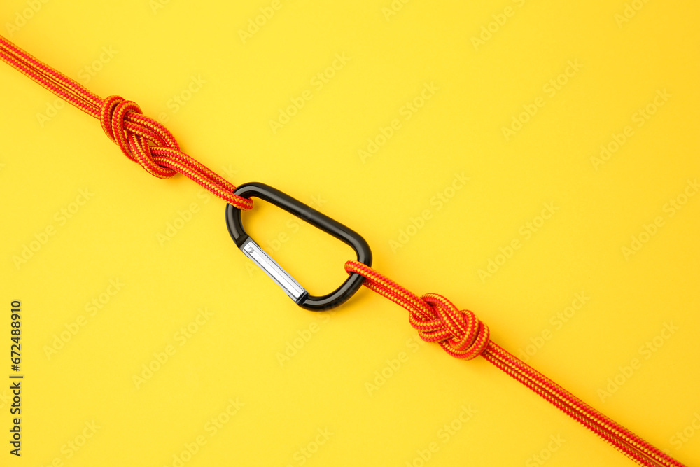 One metal carabiner with ropes on yellow background, top view One metal carabiner with ropes on yellow background, top view