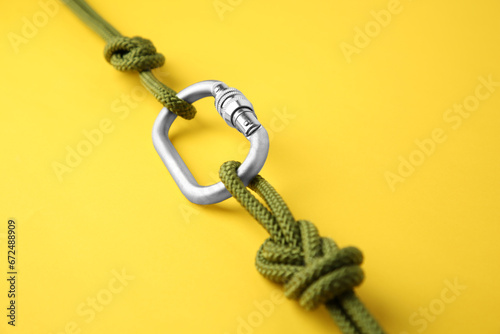 One metal carabiner with ropes on yellow background, closeup