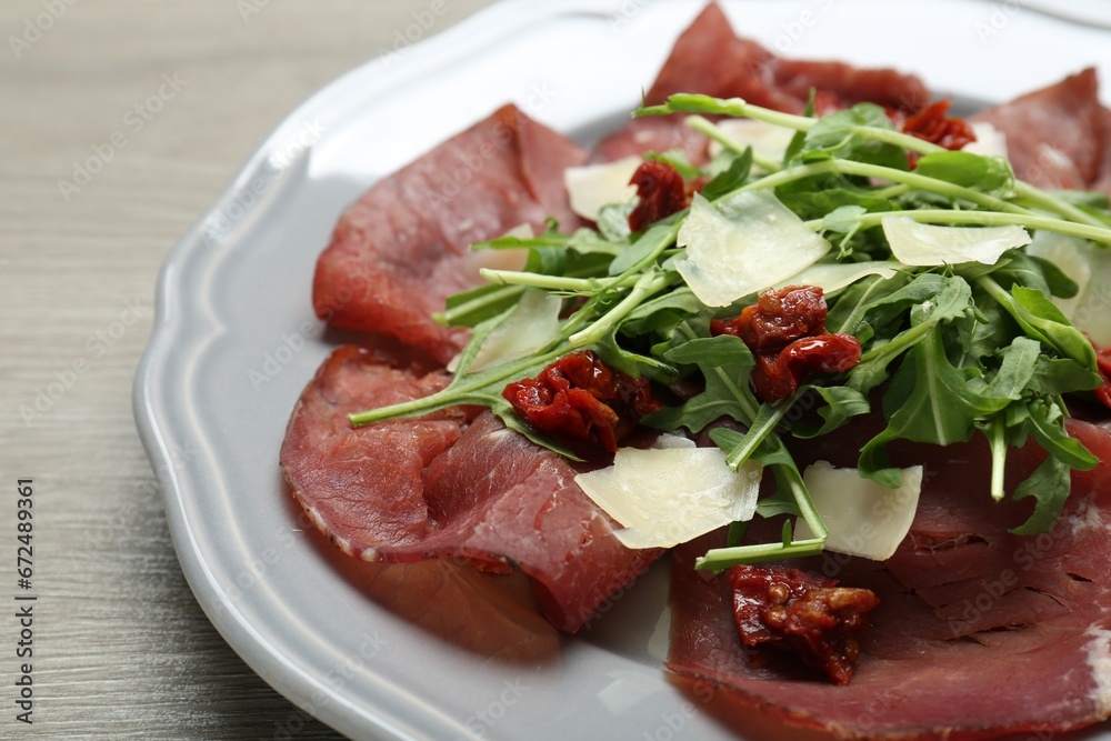 Plate of tasty bresaola salad with sun-dried tomatoes and parmesan cheese on wooden table, closeup