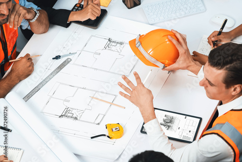 Diverse group of civil engineer and client working together on architectural project, reviewing construction plan and building blueprint at meeting table. Prudent