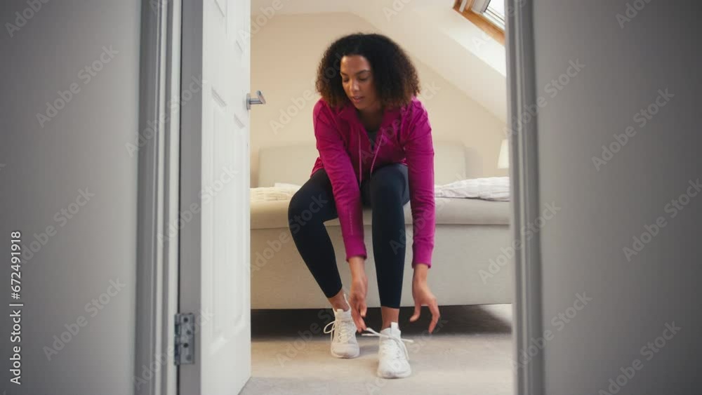 Woman in fitness clothing sitting on bed at home putting in wireless ear buds before exercise - shot in slow motion Woman in fitness clothing sitting on bed at home putting in wireless ear buds before exercise - shot in slow motion