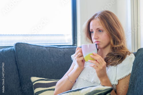 ソファーに座りマグカップのコーヒーを飲む女性（憂い）