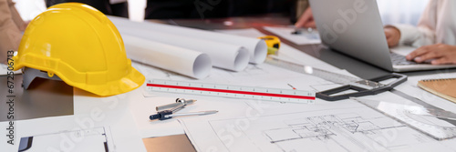 Engineer tool, architecture blueprint design and safety helmet hardhat on meeting table with contractors paper project with blurred engineer and architect working and discussing in background. Insight