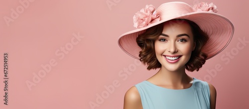 The girl wearing a bright airy dress and a hat is smiling while holding a bunch of flowers She is standing across from a woman with short hair who is wearing blue clothing against a pink bac photo
