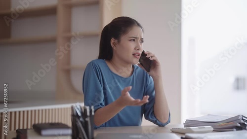 An upset and frustrated Asian woman, dressed in loungewear, is having an intense and incomprehensible phone conversation. She places the phone down with a heavy heart on her dining table.