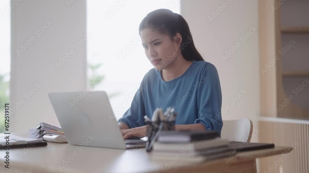 An Asian woman in loungewear looks concerned about her job and seeks solutions for a project she's struggling with. She uses her laptop at the dining table. An Asian woman in loungewear looks concerned about her job and seeks solutions for a project she's struggling with. She uses her laptop at the dining table.