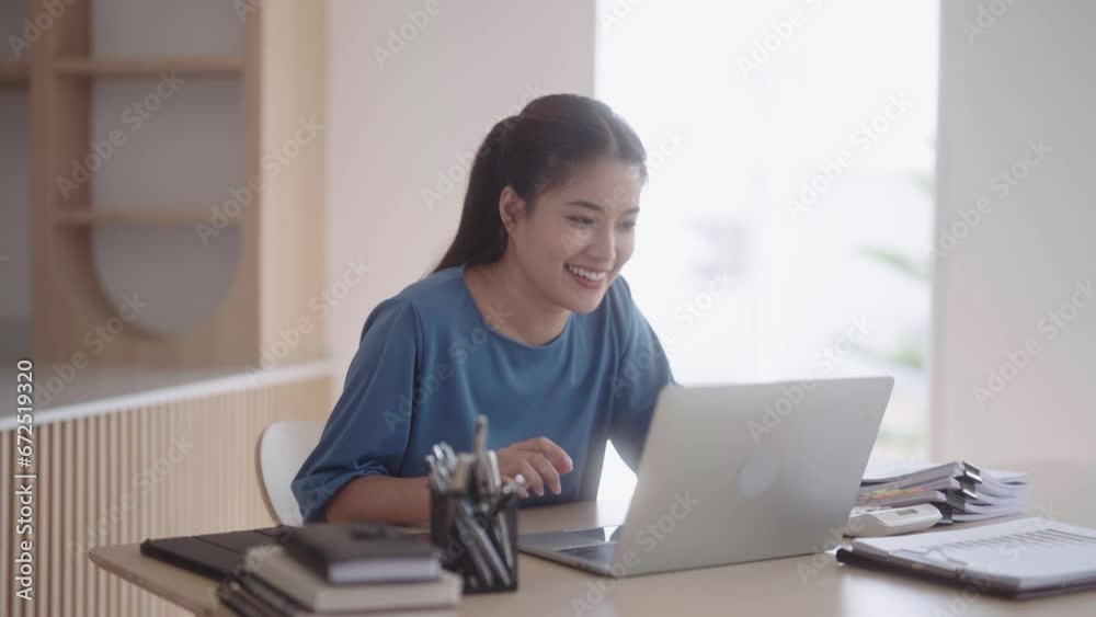 A joyful Asian woman in casual attire is delighted as she receives online exam results, confirming her successful entry into a new job. She checks her results via a laptop at her dining table. A joyful Asian woman in casual attire is delighted as she receives online exam results, confirming her successful entry into a new job. She checks her results via a laptop at her dining table.
