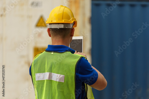 Caucasian man wearing yellow safety helmet Carrying a genuine tablet to check electrical equipment In the container storage yard
