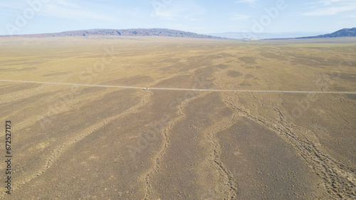 A white SUV is driving fast on a dusty road in the steppe. Clouds of dust fly from under the wheels and from the roof of the car. The jeep easily passes a dirt road. Blue sky and white clouds.