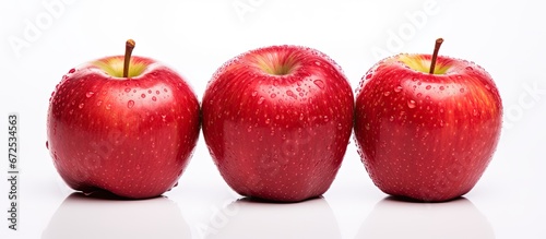 There are three apples that are red ripe and fresh placed on a white surface