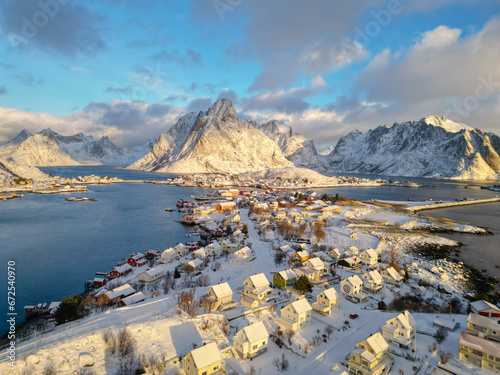 Aerial view of Lofoten island Norway. The winter season of sunrise fishing village of Reine with snowscape mountain peak reflect on water. Norway with red rorbu houses. With falling snow in winter. photo