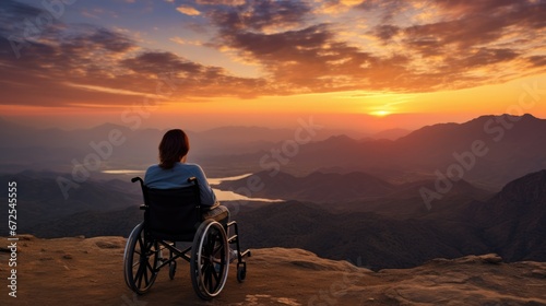 Woman with disability sitting on a wheelchair enjoying sundown on mountain background.