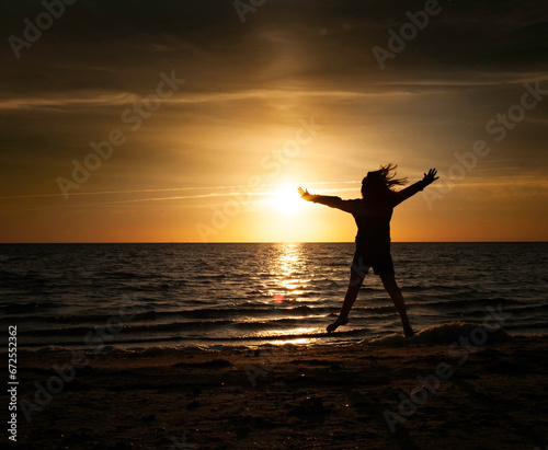 Silhouette of young girl jumping at beach at sunset photo