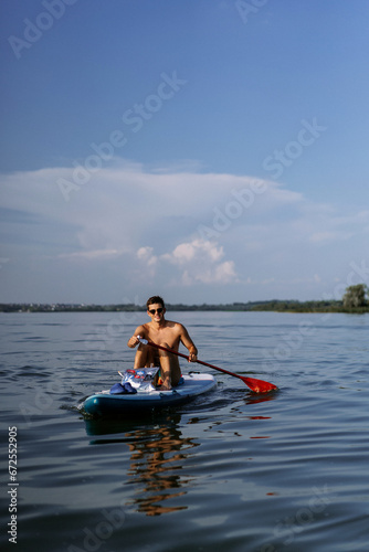 Man in swimming trunks rides paddleboard on a lake in summer. supboard