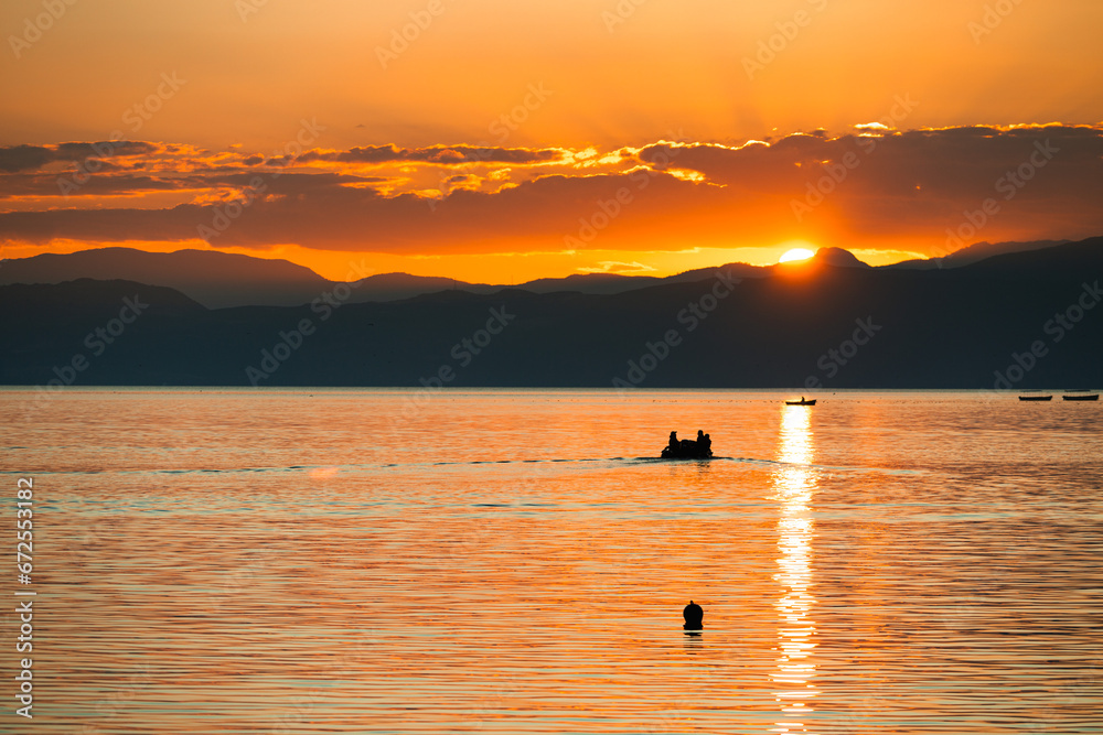 Motorized dinghy sailing toward the sun in silhouette
