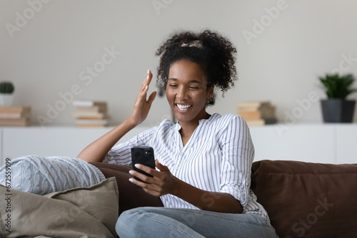 Happy joyful millennial Black girl making video call on smartphone, enjoying conference talk, reading funny text message, speaking and laughing, looking at screen, mobile phone webcam, feeling joy