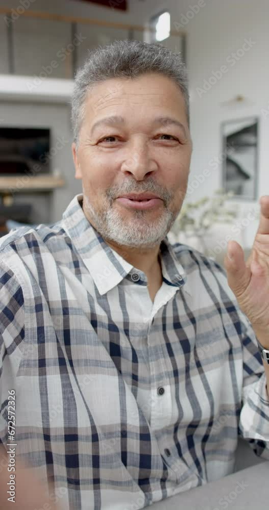 Vertical video of happy senior biracial man discussing and gesticulating at home