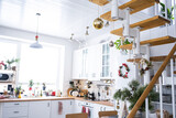 Festive Christmas decor in white kitchen, white modern loft interior with a metal modular ladder with wooden steps. New Year, mood, cozy home.