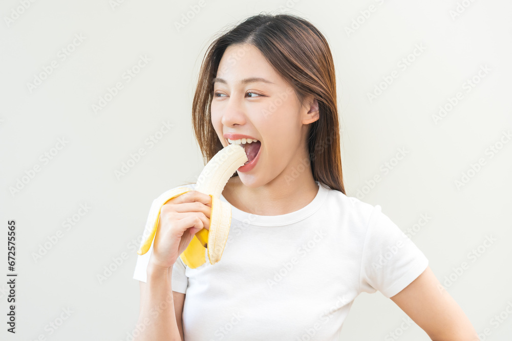 Healthy of tropical fruit in summer concept, beautiful happy asian young woman eating, biting fresh ripe banana, smile girl get energy, vitamin from natural organic food. isolated on white background. Healthy of tropical fruit in summer concept, beautiful happy asian young woman eating, biting fresh ripe banana, smile girl get energy, vitamin from natural organic food. isolated on white background.