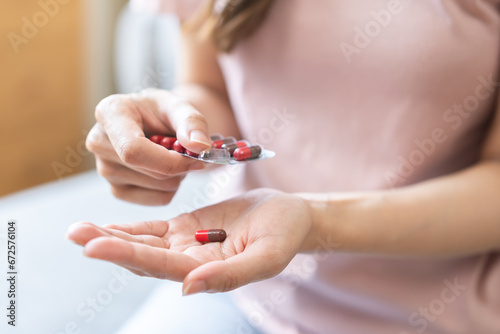 Sick ill asian young woman, girl hand taking tablet pill capsule out from blister pack, painkiller medicine from stomach pain, head ache, pain for treatment, take drug or vitamin at home, health care. photo