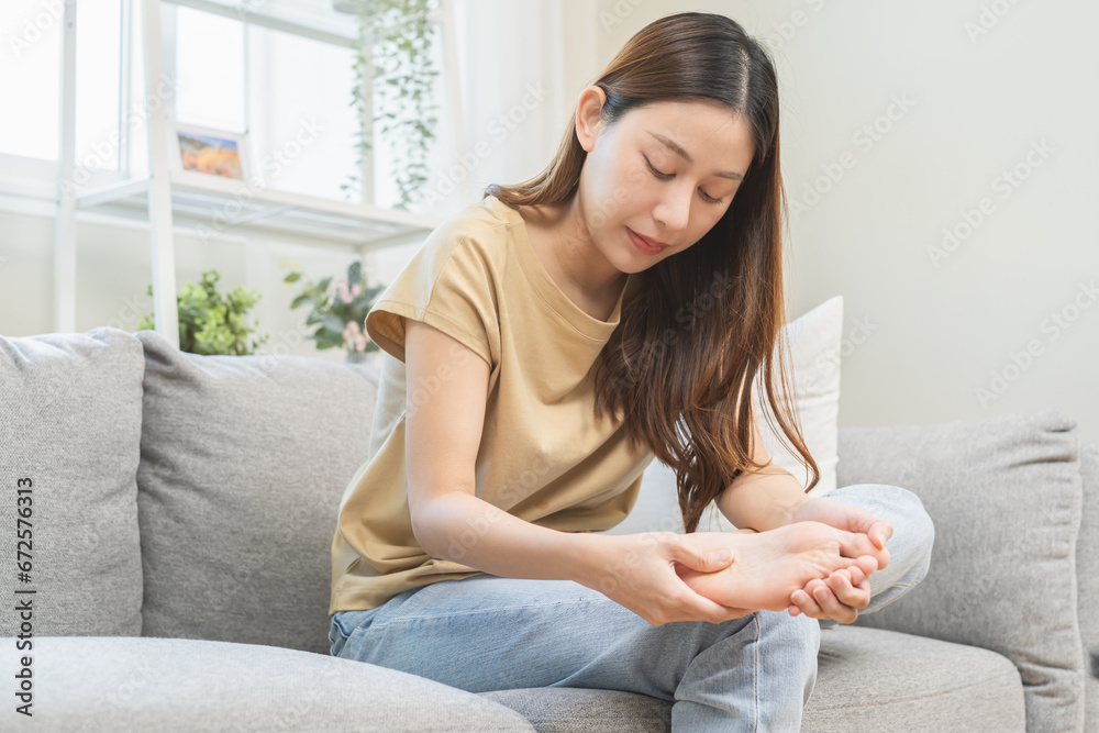 Health care foot pain, suffering asian young woman hand rubbing, massaging sore feet area pain, sitting on sofa at home. Discomfort painful feet ache from walking for long. Physical injury. Health care foot pain, suffering asian young woman hand rubbing, massaging sore feet area pain, sitting on sofa at home. Discomfort painful feet ache from walking for long. Physical injury.