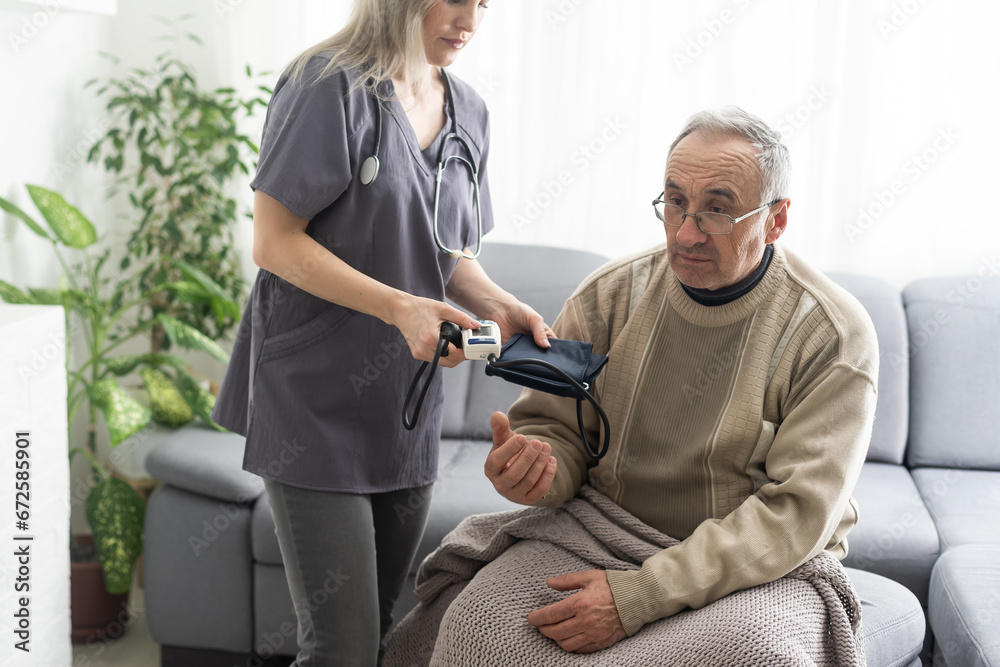 Obraz premium Smiling young nurse taking old man's blood pressure