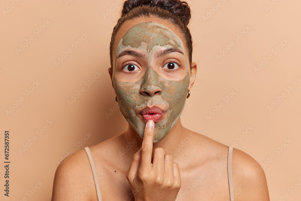 Young beautiful woman with nourishing clay mask on face keeps lips