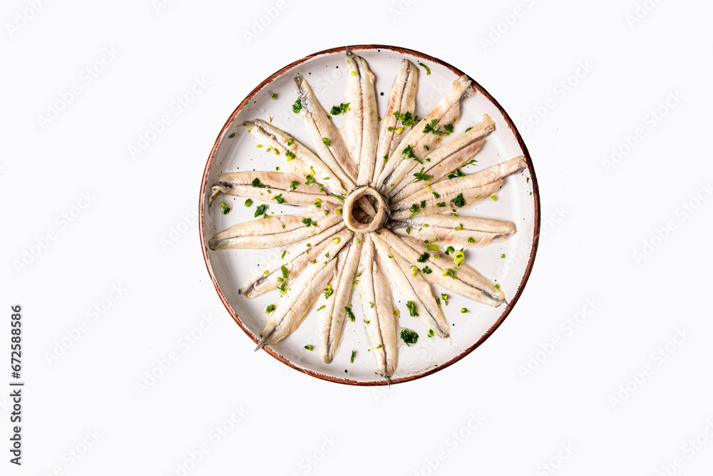 Pickled anchovies with garlic and parsley on a round rustic plate and white background, top view. Pickled anchovies with garlic and parsley on a round rustic plate and white background, top view.