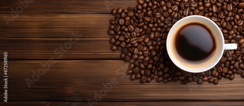 On a wooden table there is a cup filled with coffee and a few coffee beans scattered nearby
