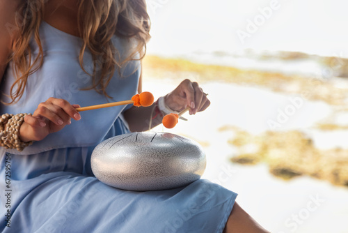 Close up of woman hands play relaxing melody on hapi steel tongue drum on seaside. Perfect lady playing relax music at tropical beach. Tropic summer vacation, meditating concept. Copy ad text space photo