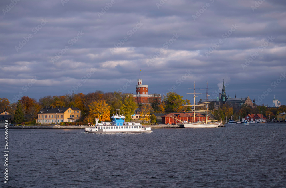 View at the bay strömmen with inner harbor commuter ferry passing the castle on the island Kastellholmen, grey sky back ground and low morning sun light, early autumn morning in Stockholm