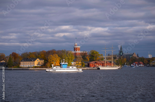 View at the bay strömmen with inner harbor commuter ferry passing the castle on the island Kastellholmen, grey sky back ground and low morning sun light, early autumn morning in Stockholm