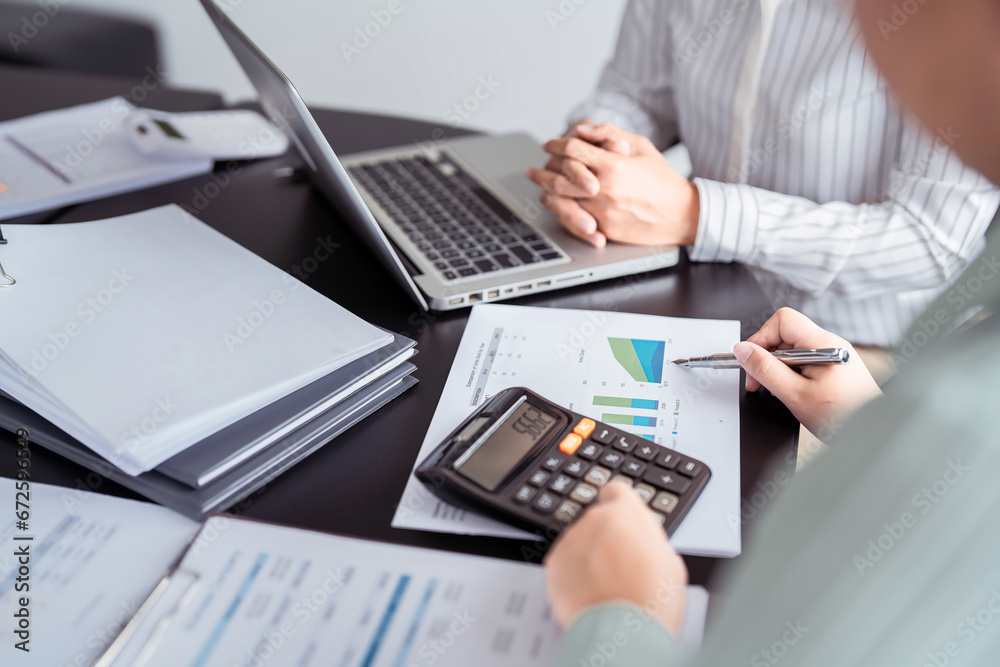 Two business real estate seller using calculator to calculating about property investment and pointing on document to explaining terms data about home sales contract and home insurance in office Two business real estate seller using calculator to calculating about property investment and pointing on document to explaining terms data about home sales contract and home insurance in office